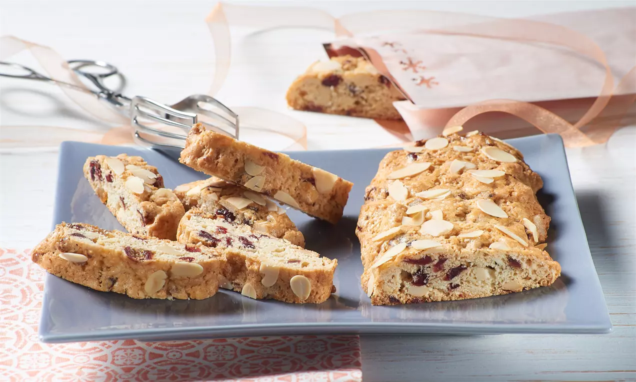 Knusprige Biscotti mit goldbrauner Kruste, gespickt mit Mandelsplittern und getrockneten Früchten, auf einem blauen Teller arrangiert