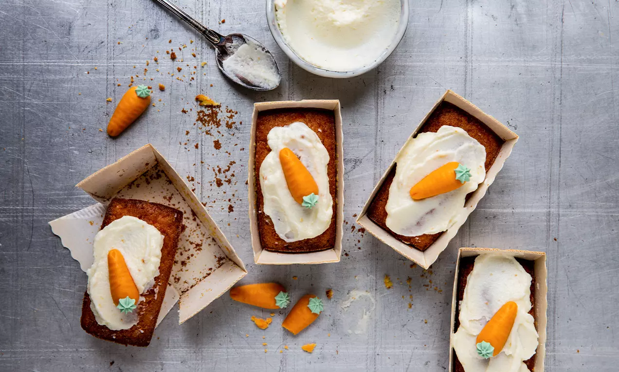 Minicakes rectangles dorés à la carotte garnis de crème blanche lisse et décorés de petites carottes en pâte d’amande orange