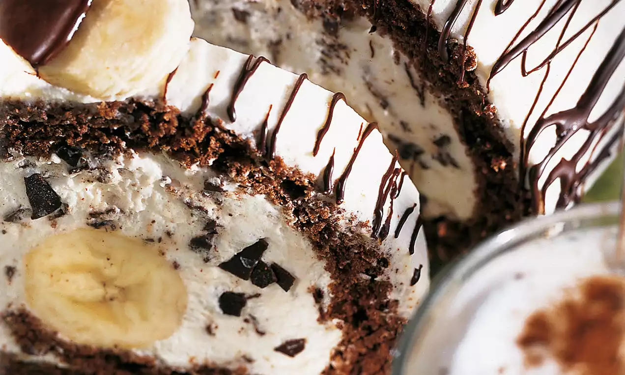Rotolo al cioccolato scuro con ripieno cremoso puntinato di scaglie, fette di banana e decorazioni di glassa al cioccolato a strisce sottili