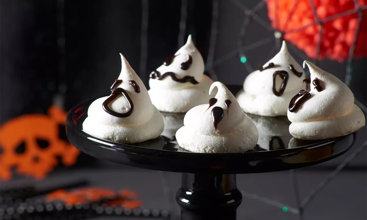 Petits fantômes en meringue blanche brillante, torsadés et décorés de filaments de chocolat noir sur un plateau noir élégant