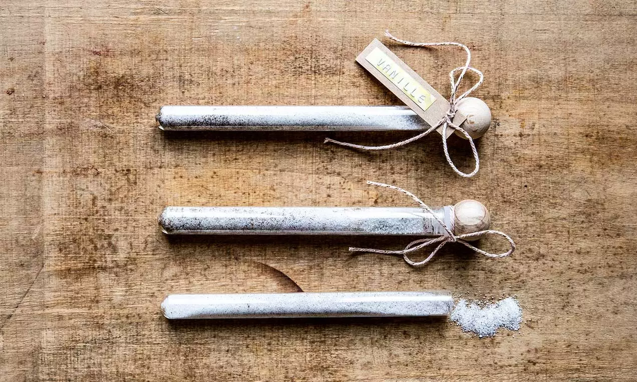 Fialette di vetro trasparente riempite di sale vanigliato bianco, chiuse con tappi di legno naturale e legate con spago sottile su tavola di legno