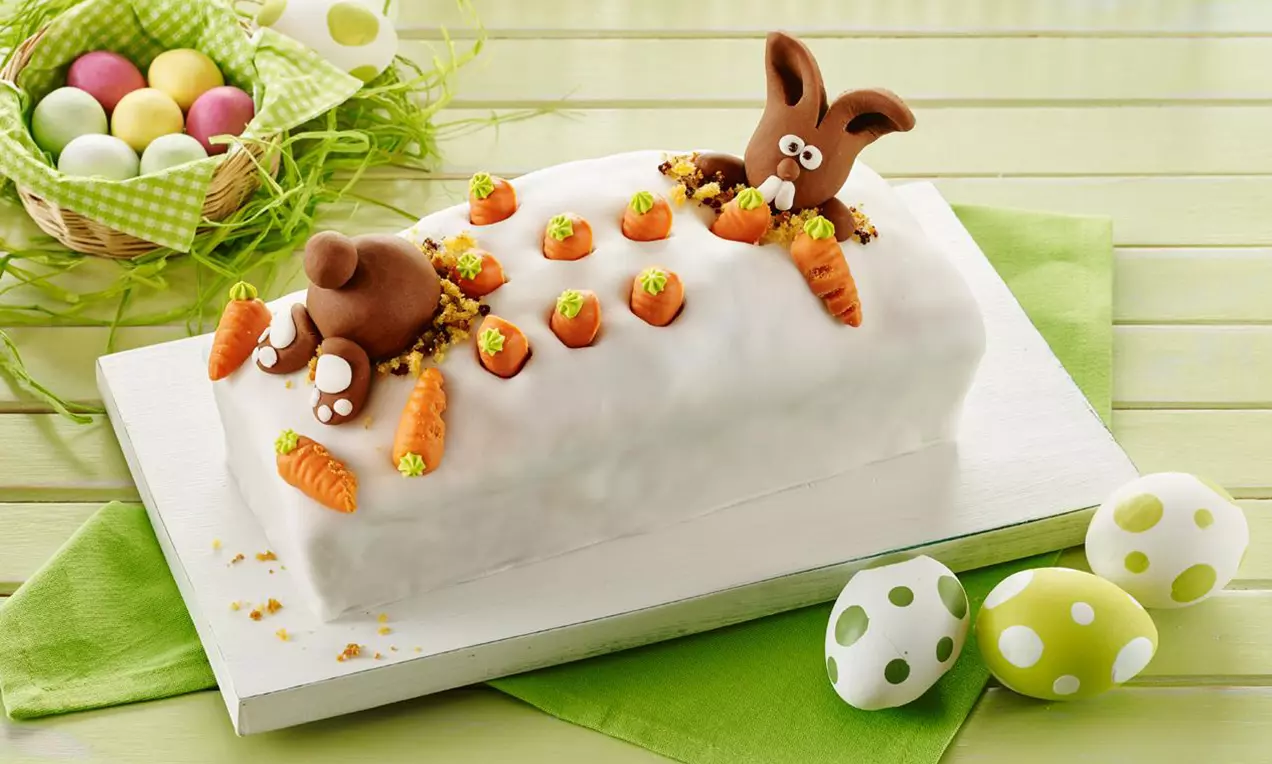 Cake marbré blanc recouvert de fondant avec des lapins en chocolat brun et des carottes en pâte colorée sur une planche blanche