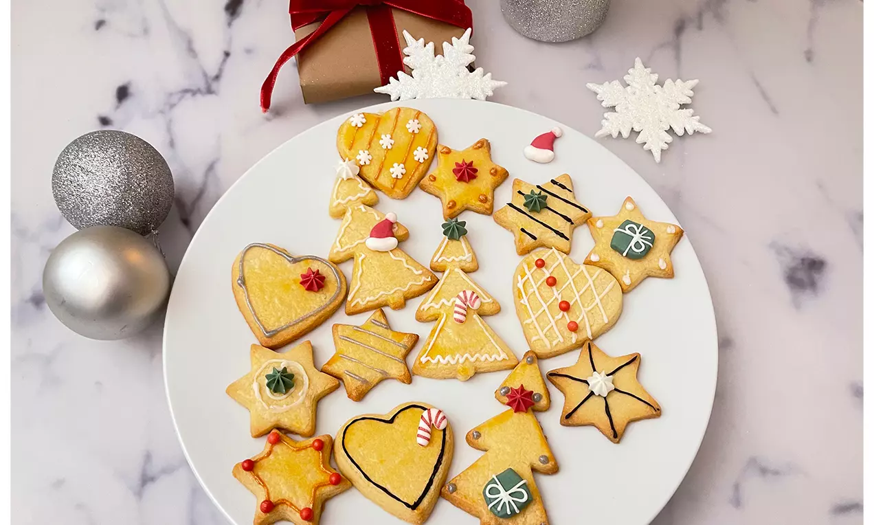 Biscuits dorés en forme de cœurs, étoiles et sapins décorés de glaçage coloré sur une assiette blanche avec décorations festives