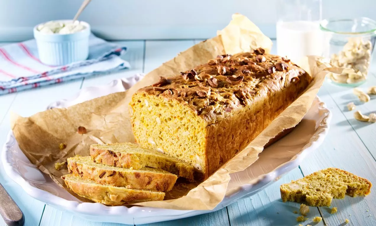 Goldgelbes Curry Brot mit lockerer Krume, Kürbiskernen und Cashewstücken auf braunem Backpapier und weißer Platte angeschnitten arrangiert
