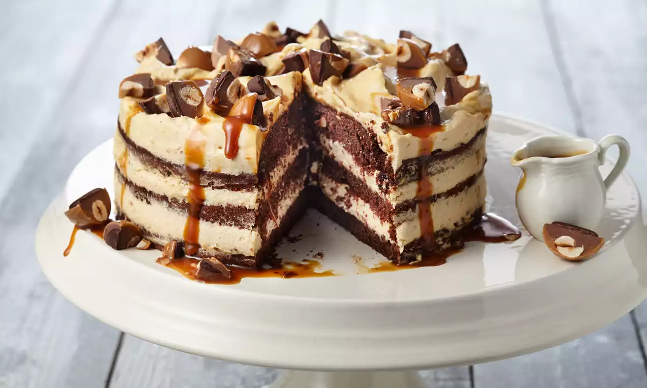 Mehrschichtige Karamelltorte mit goldener Creme, Schokoladenschichten, Toffifee-Stückchen und Karamellsoße auf weißer Tortenplatte