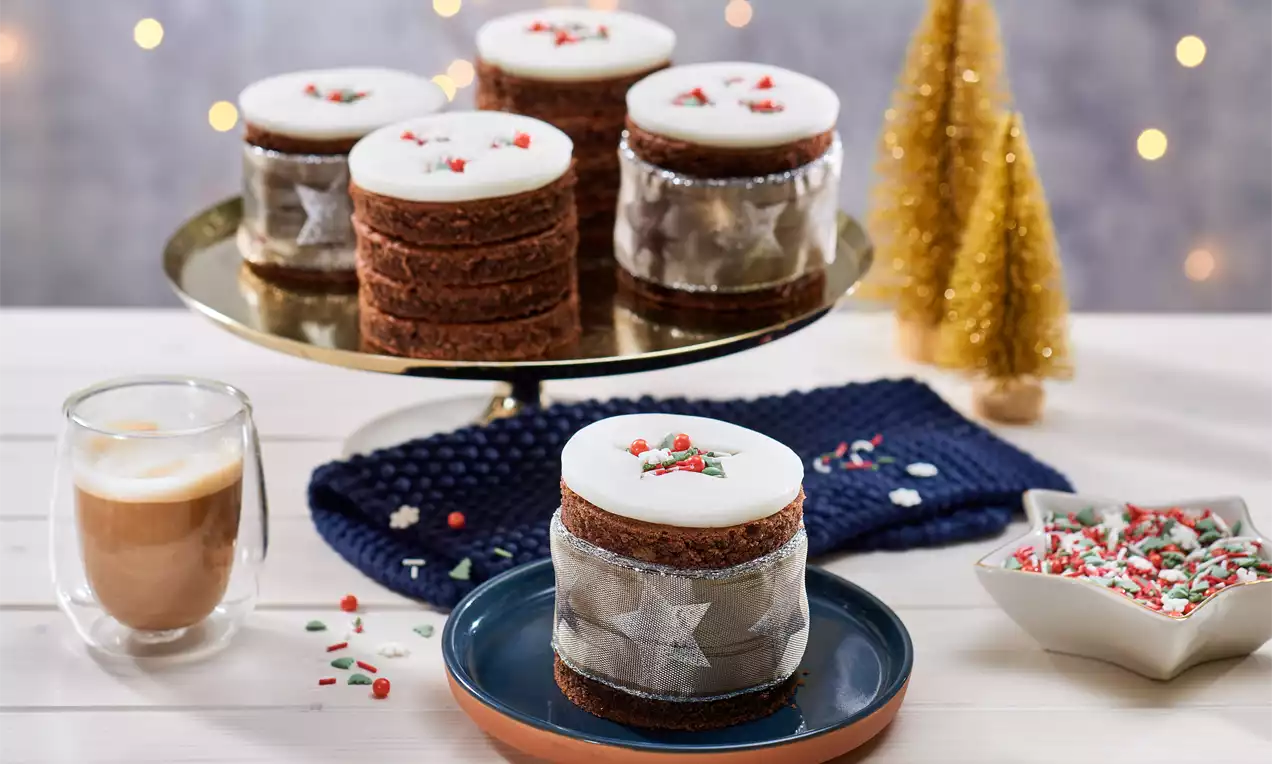 Mini-gâteaux de Noël bruns en couches avec un glaçage blanc décoré de perles rouges et vertes sur des assiettes et un plateau doré