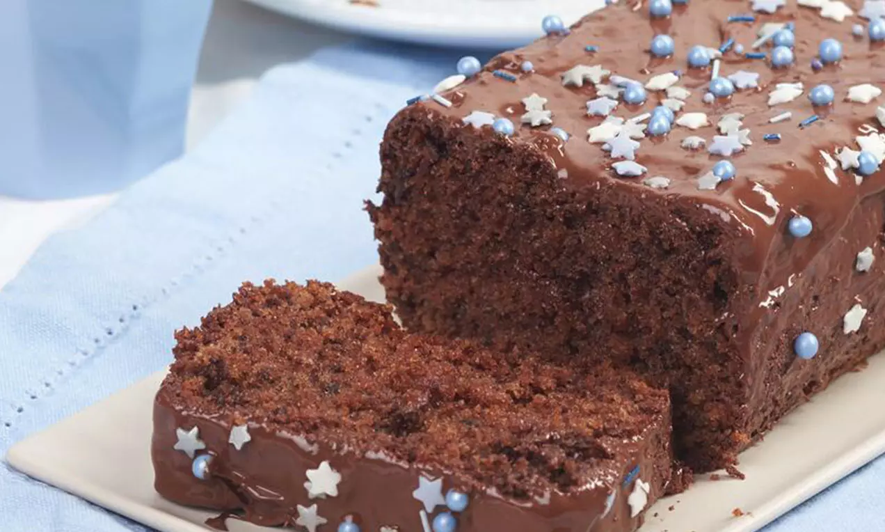 Gâteau rectangulaire moelleux au chocolat foncé couvert de glaçage Nutella® brillant décoré de perles bleues et étoiles blanches sur un plateau