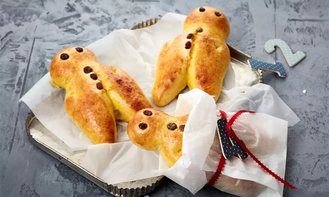 Petit bonhommes dorés en pâte levée moelleuse ornés de pépites de chocolat, disposés sur du papier blanc dans un plat argenté
