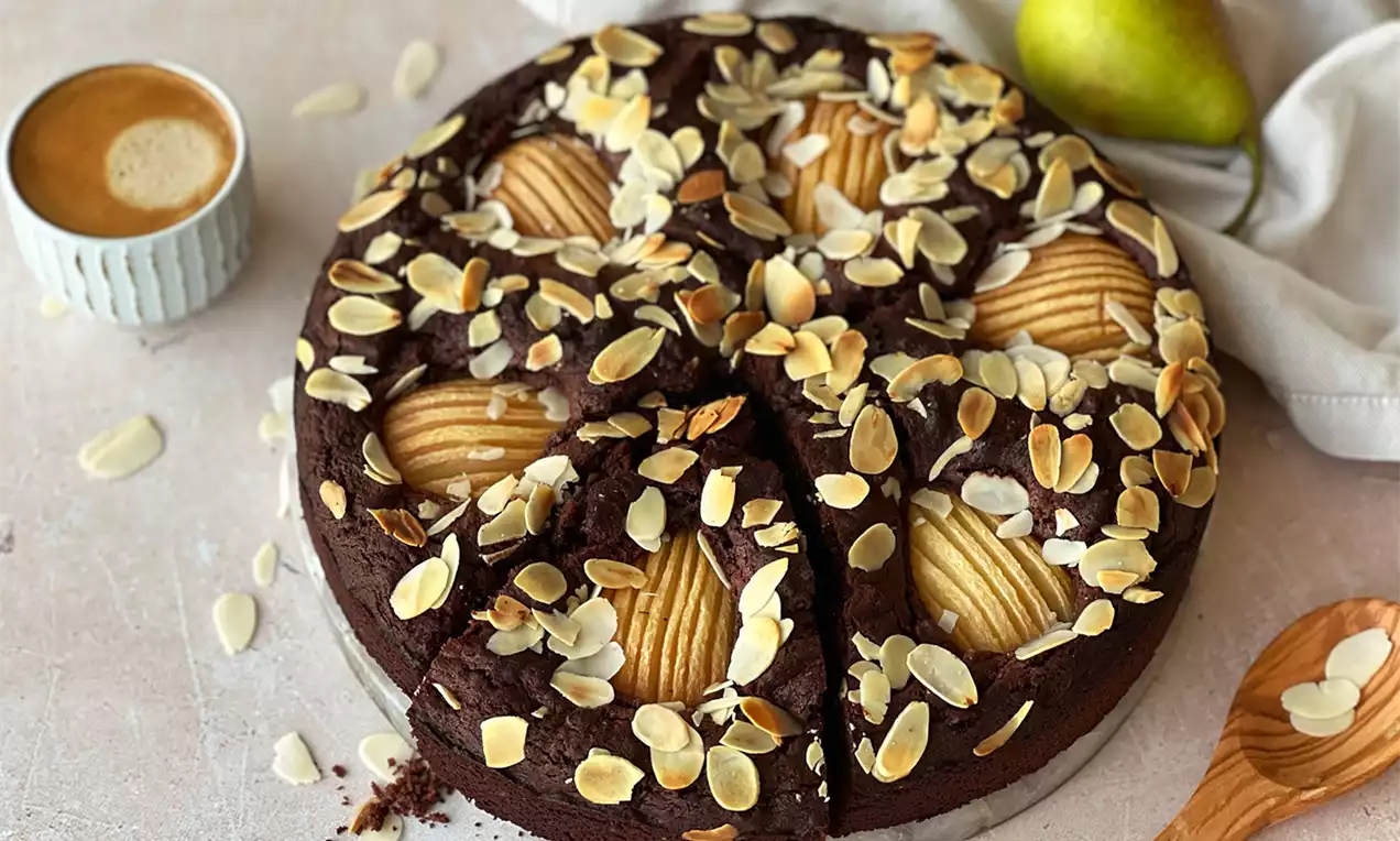 Runder Schokoladenkuchen mit saftigen, halbierten Birnen und goldbraunen Mandelblättchen, serviert auf einem hellen Untergrund