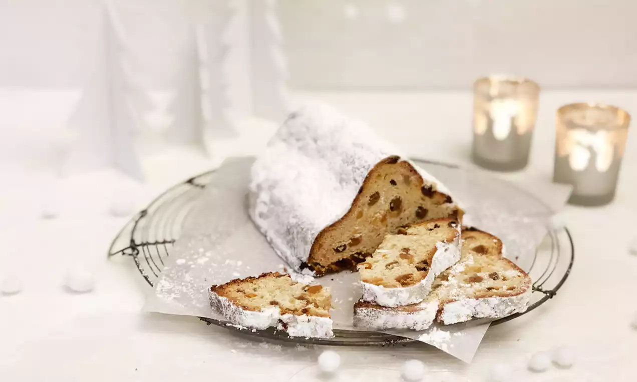Ein Quarkstollen mit goldgelber Kruste und rosinenreicher Füllung, bestäubt mit weißem Puderzucker auf Backpapier auf einem Gitter