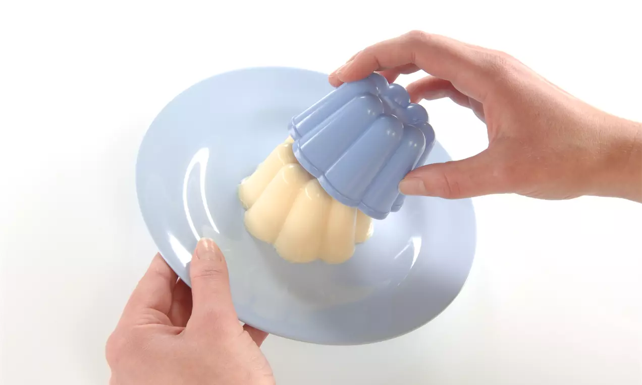 Vanillefarbener Pudding mit glatter Oberfläche wird aus einer blauen Kunststoffform auf einen hellblauen Teller gestürzt