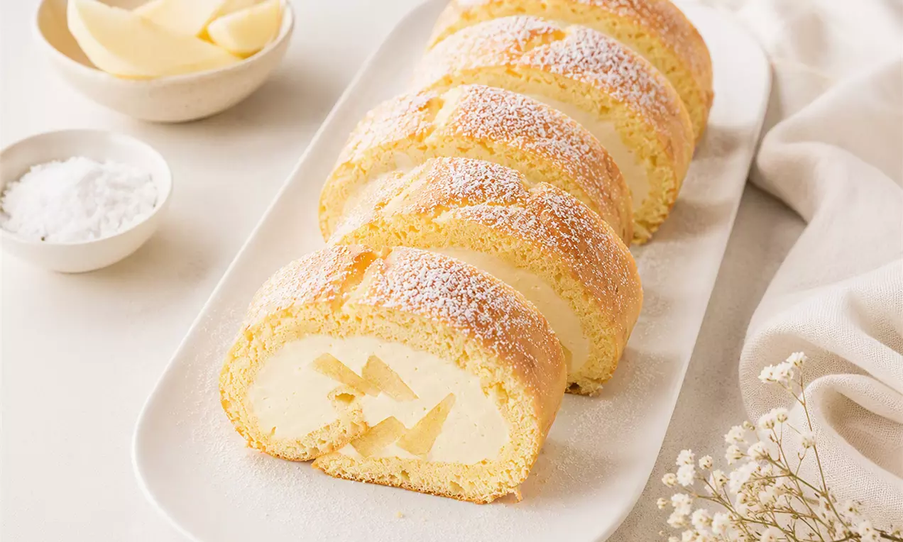 Goldgelbe Apfelroulade mit lockerer Füllung, in Scheiben geschnitten, auf einer weißen Platte mit Puderzucker bestäubt und zart dekoriert, AI-labeled image