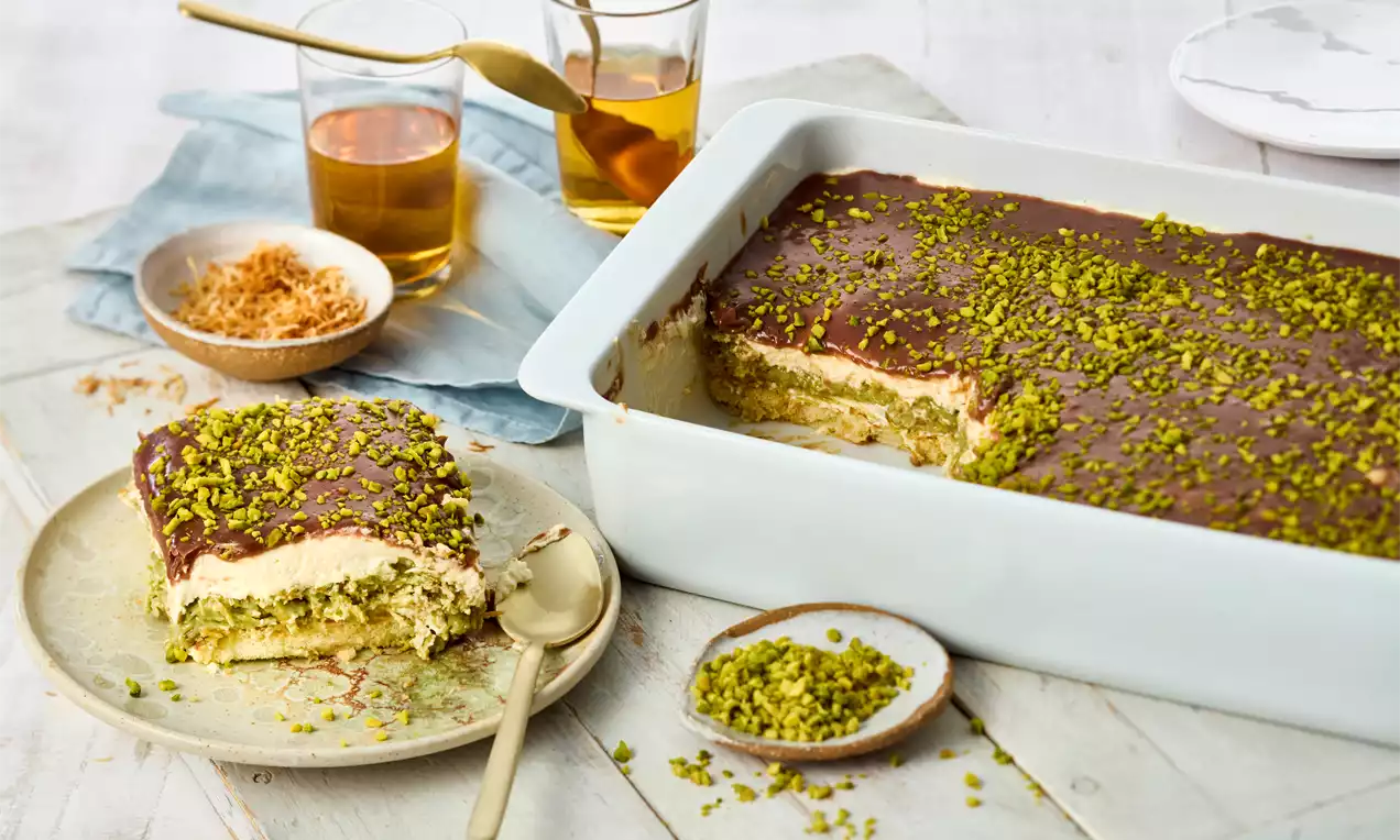 Dubai Chocolate Tiramisu mit glänzender Schokocreme, heller Füllung und grünen Pistazienstückchen in weißer Form, angerichtet mit Beilagen