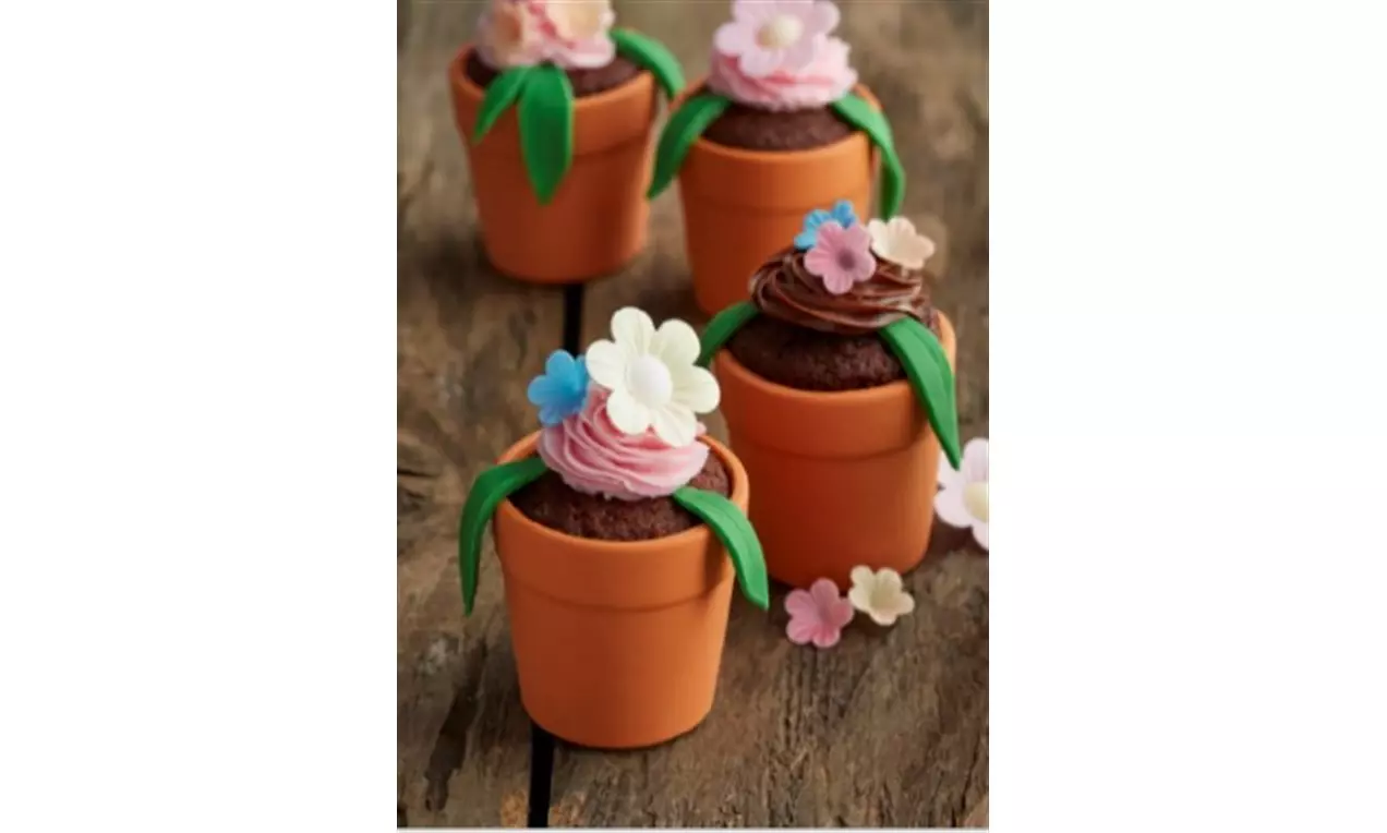 Cupcake al cioccolato in vasetti di terracotta con crema dai toni rosa e marroni decorata con fiori color pastello e foglie verdi di zucchero