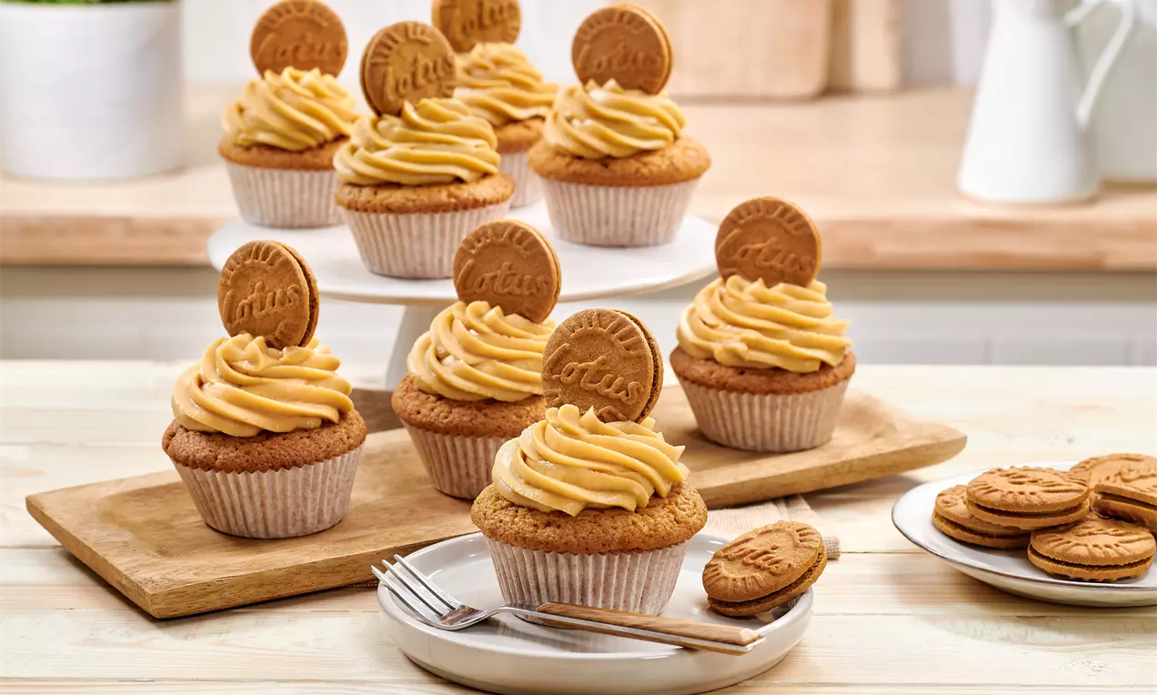 Cupcakes mit goldbrauner Biskuitbasis und karamellfarbener Cremehaube, garniert mit Lotus-Keksen, auf Holzbrett und weißem Teller arrangiert