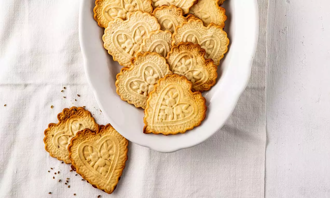 Biscuits en forme de cœur légèrement dorés avec des motifs en relief complexes, présentés dans une assiette blanche sur une nappe blanche