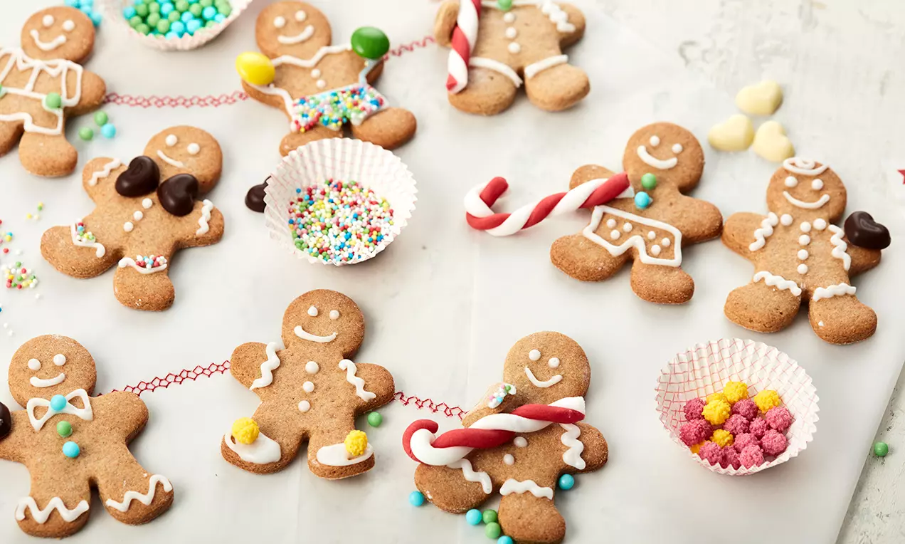 Lebkuchenmänner in Braunton mit weißem Zuckerguss verziert, garniert mit bunten Streudekoren und kleinen Süßigkeiten auf Backpapier arrangiert