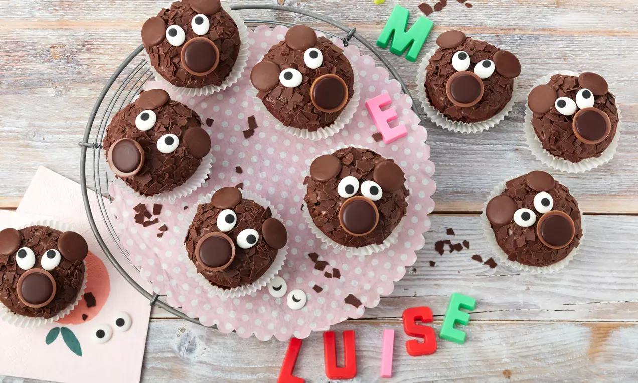 Schokoladen-Muffins mit brauner Krümeltextur, dekoriert mit Augen aus Zucker und Ohren aus Schokolade auf rosa gepunktetem Papier
