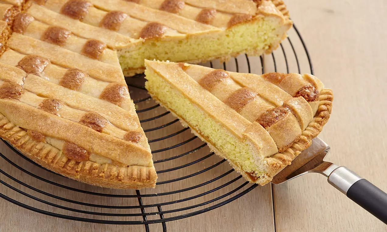 Tarte ronde dorée avec un motif quadrillé en pâte croustillante, garniture moelleuse jaune clair, posée sur une grille noire