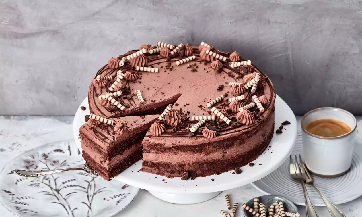 Schoko-Torte mit cremiger Textur, geschichtetem Teig, dekoriert mit Streifen-Schokoröllchen und Tupfen auf weißer Tortenplatte