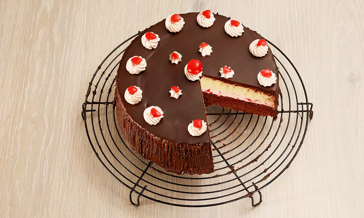 Torta rotonda con glassa di cioccolato scuro, decorata con ciuffi di panna bianca e ciliegie rosse su una griglia metallica nera