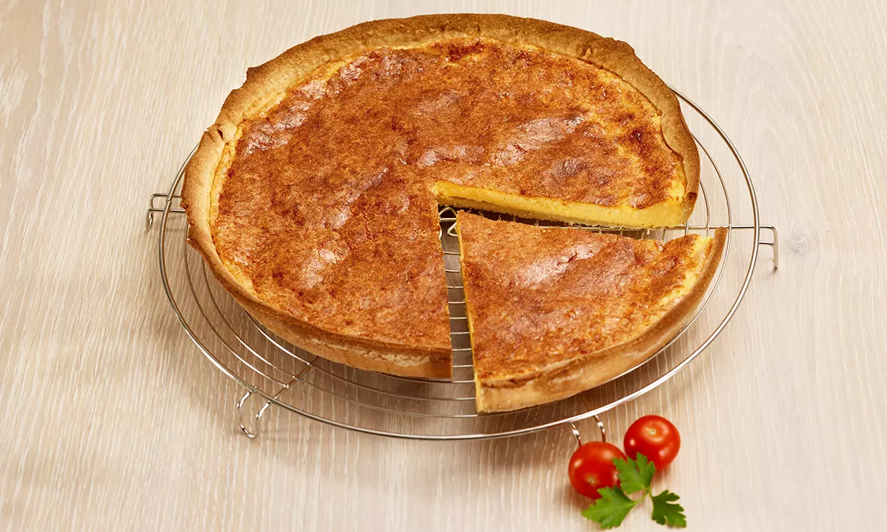 Tarte dorée à la croûte légèrement croustillante et garniture crémeuse au fromage, présentée sur une grille avec des tomates cerises et du persil