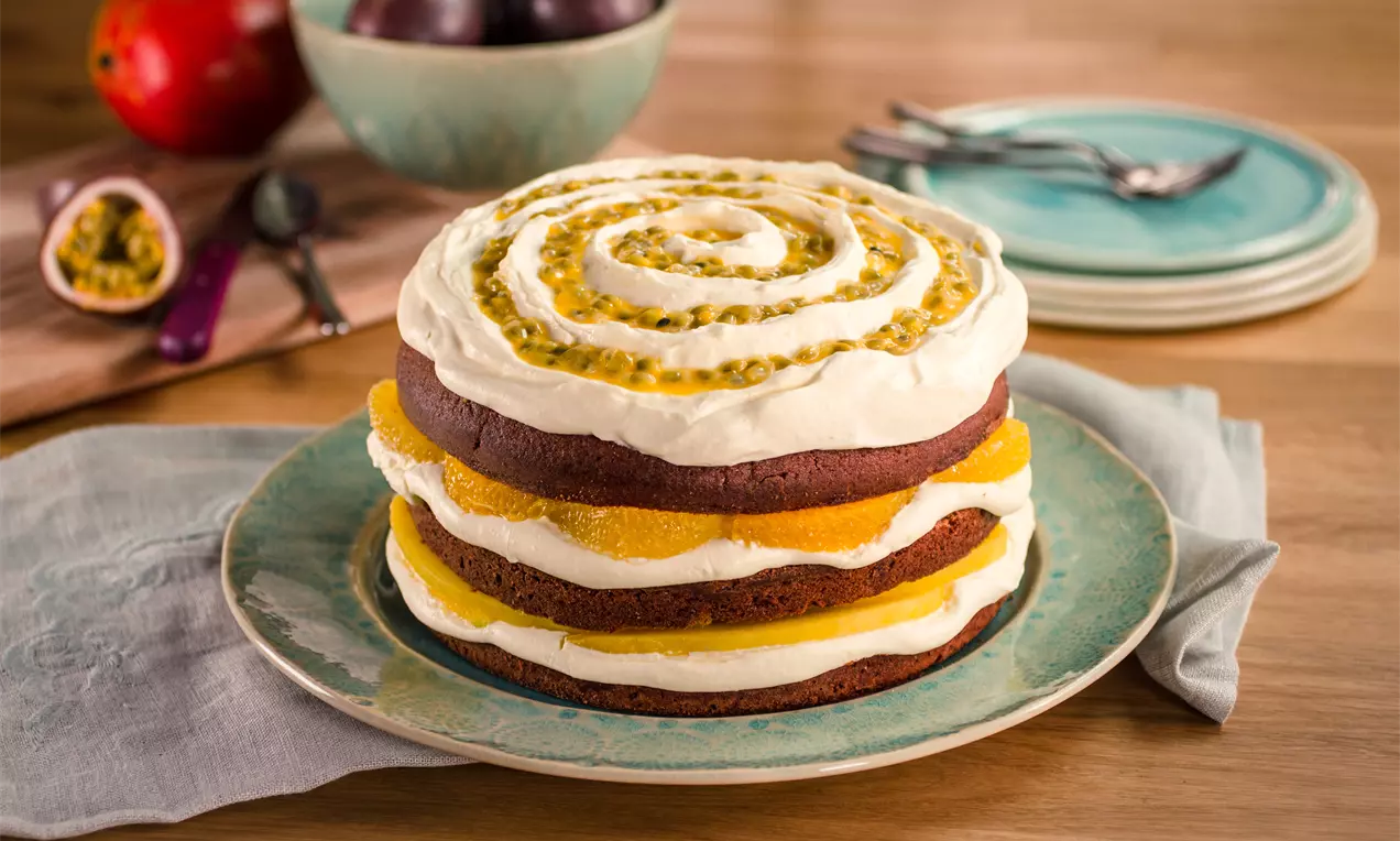 Dunkler Naked Cake mit Schichten aus saftigem Schokoteig, weißer Creme, Orangenscheiben und Passionsfruchtstreifen auf türkisfarbenem Teller
