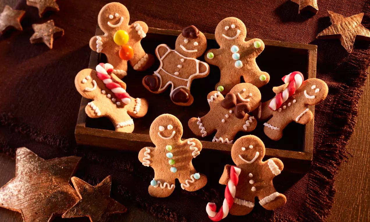 Biscotti a forma di omini di pan di zenzero marrone, decorati con glassa bianca e colorata, disposti in una scatola su fondo caldo marrone