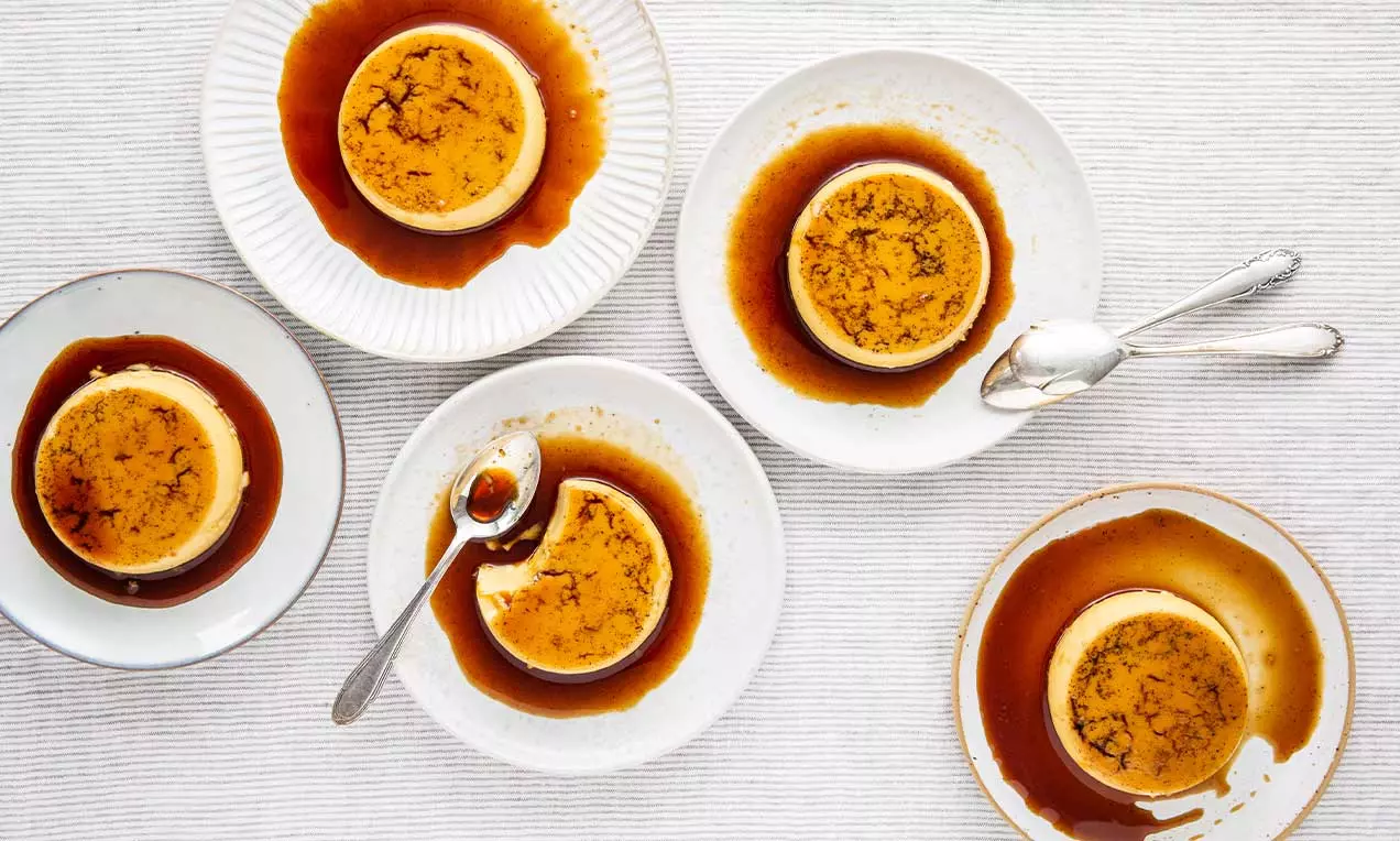 Petits flans dorés nappés de caramel ambré sur des assiettes blanches, accompagnés de cuillères argentées sur une nappe rayée