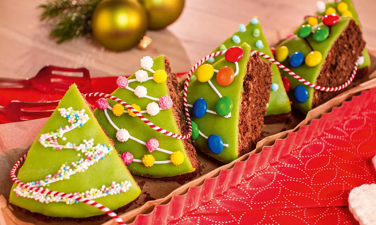 Schokoladen-Tannenbäumchen mit grüner Glasur, bunt dekoriert mit Zuckerkugeln und Streifen aus Zuckergarn auf rotem Untergrund