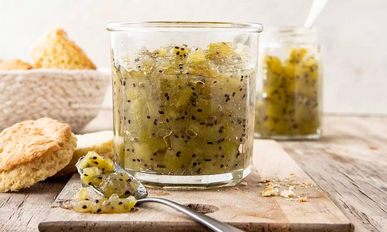 Confettura di kiwi verde brillante con semi neri visibili, dalla consistenza morbida e lucida, servita in barattoli di vetro su un tavolo di legno