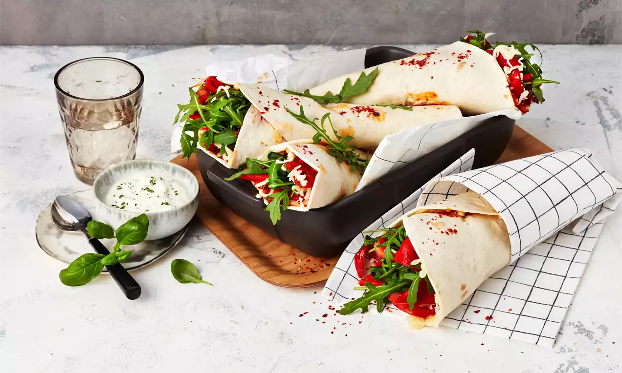 Pizza-Wraps mit goldbraunen Fladen, frischen roten Paprikastreifen, grünem Rucola und weißem Käse, angerichtet in einer schwarzen Schale