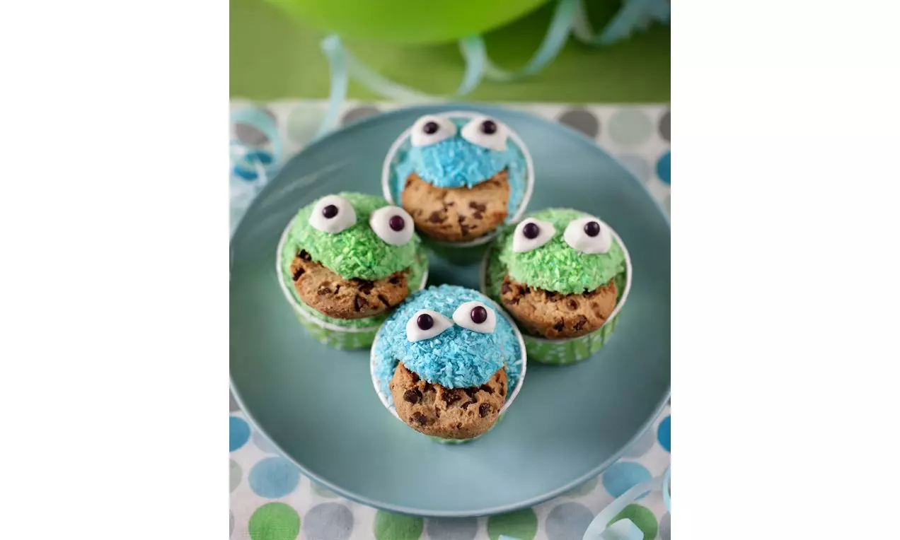 Muffins aux couleurs vives bleu et vert avec des yeux en sucre et une texture moelleuse, garnis de biscuits chocolat sur une assiette turquoise