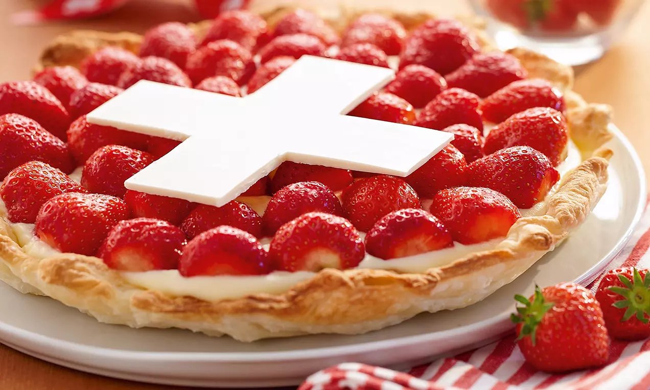 Tarte à la pâte dorée garnie de fraises brillantes disposées en cercle, décorée d'une croix blanche sur une assiette blanche