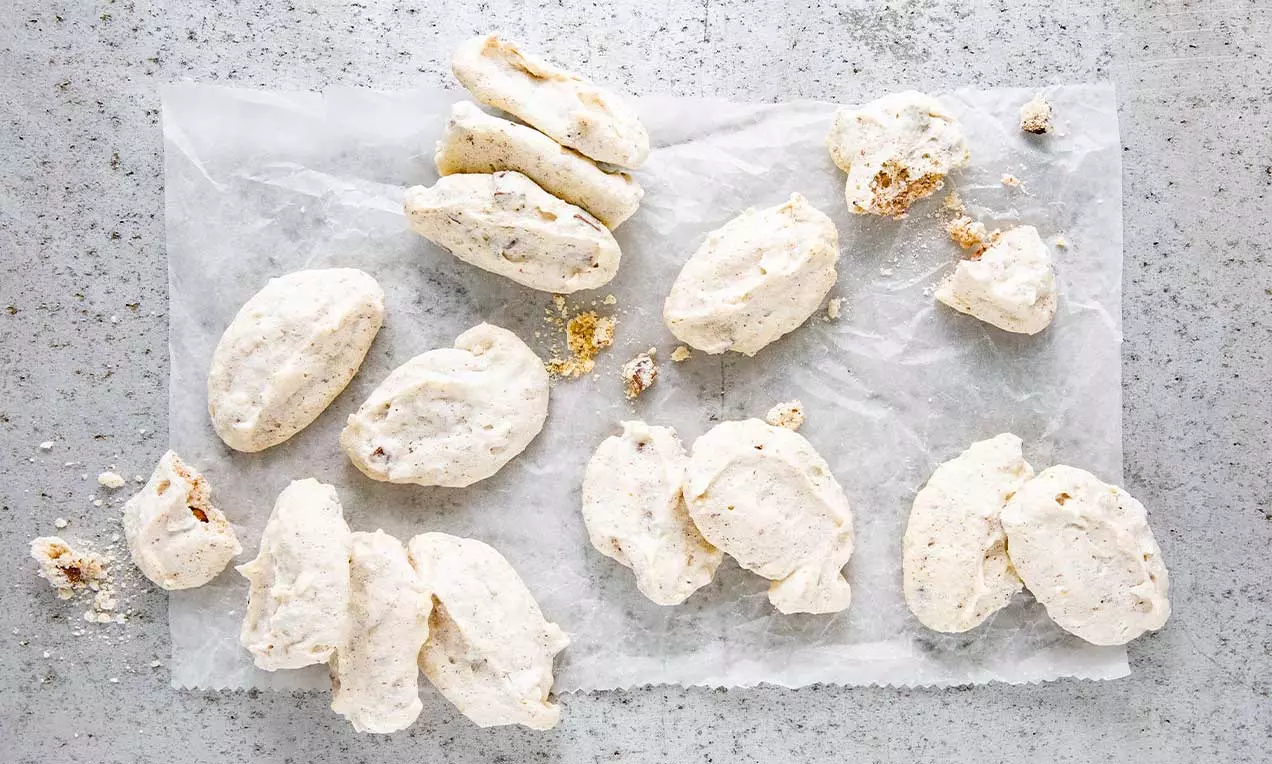 Petits amas blancs cassants à la texture aérienne, parsemés de morceaux dorés, disposés sur un papier parchemin translucide