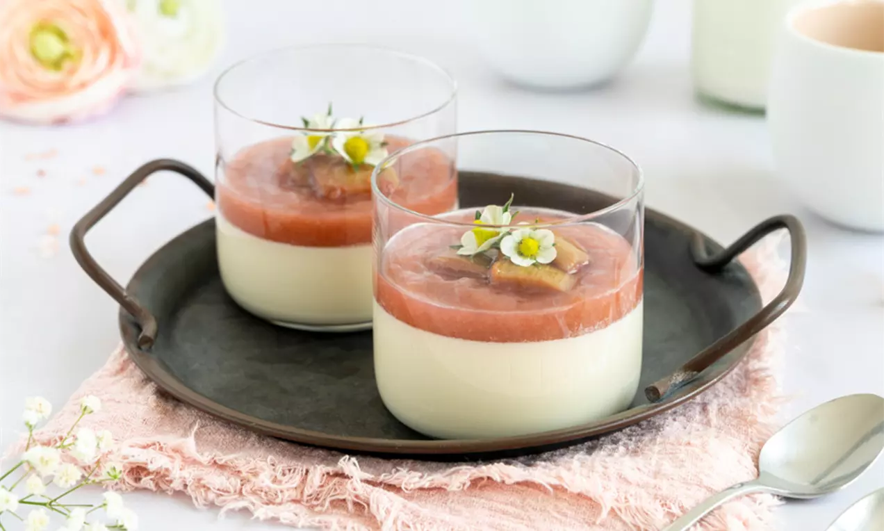 Rhabarber-Panna-Cotta in klaren Gläsern mit rosafarbenem Rhabarberkompott, filigranen Blüten und serviert auf dunkelgrauem Tablett