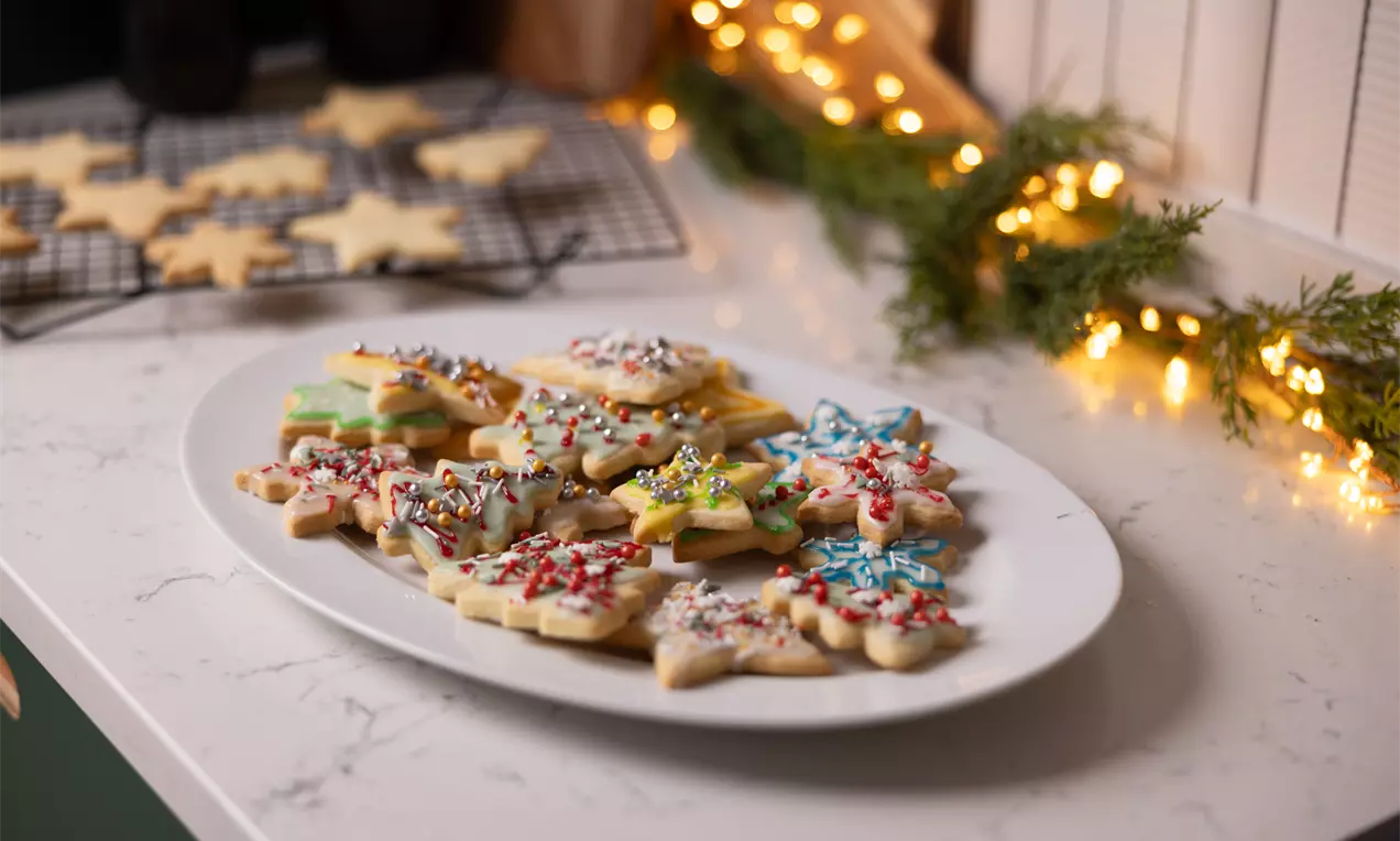 Biscuits de Noël en forme d'étoiles colorées, glacés et décorés de perles et paillettes sucrées sur une assiette blanche posée sur une table en marbre