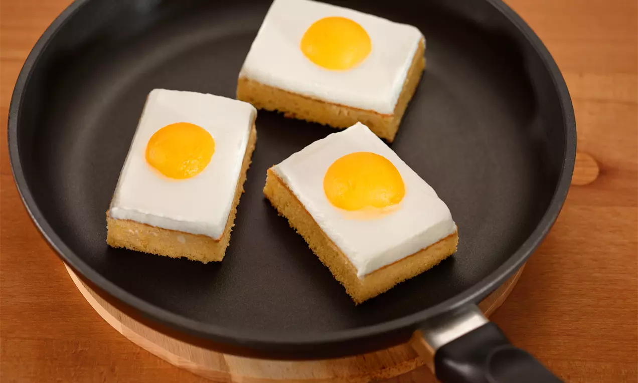 Tranches rectangulaires dorées surmontées d’une crème blanche lisse et d’un disque jaune vif, disposées dans une poêle noire